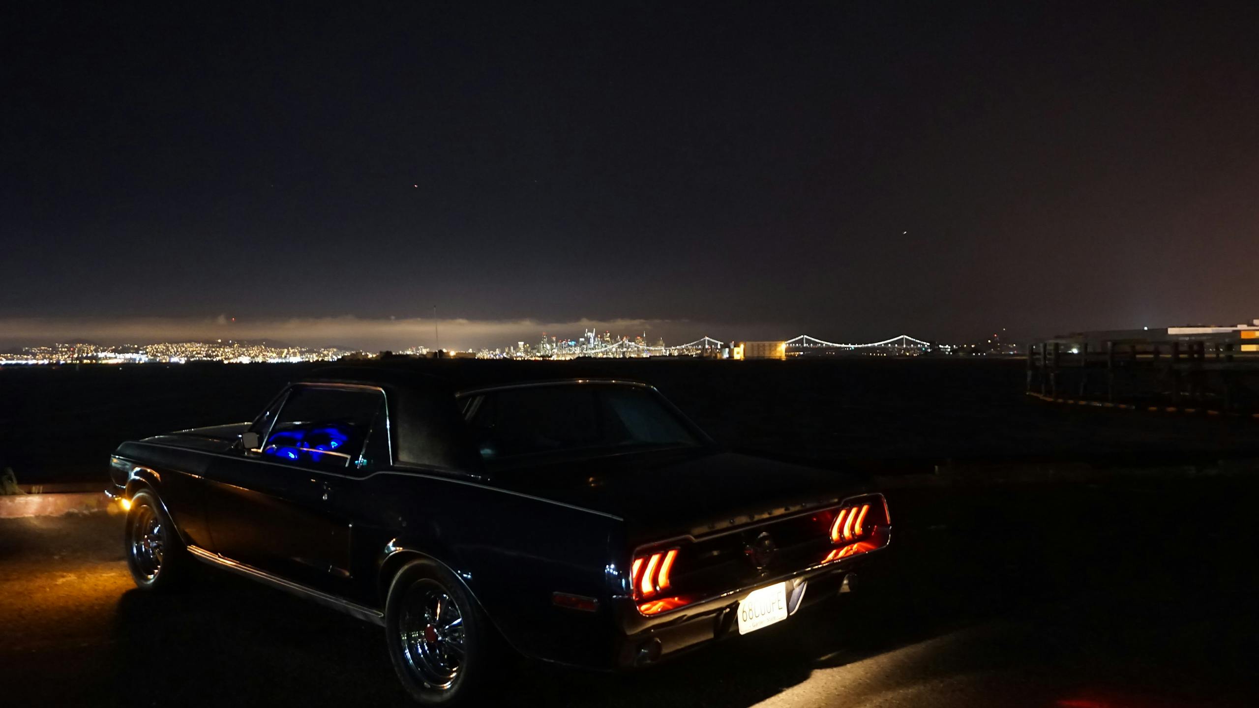 Iconic Mustang parked by the waterfront with city skyline and bridge illuminated at night.