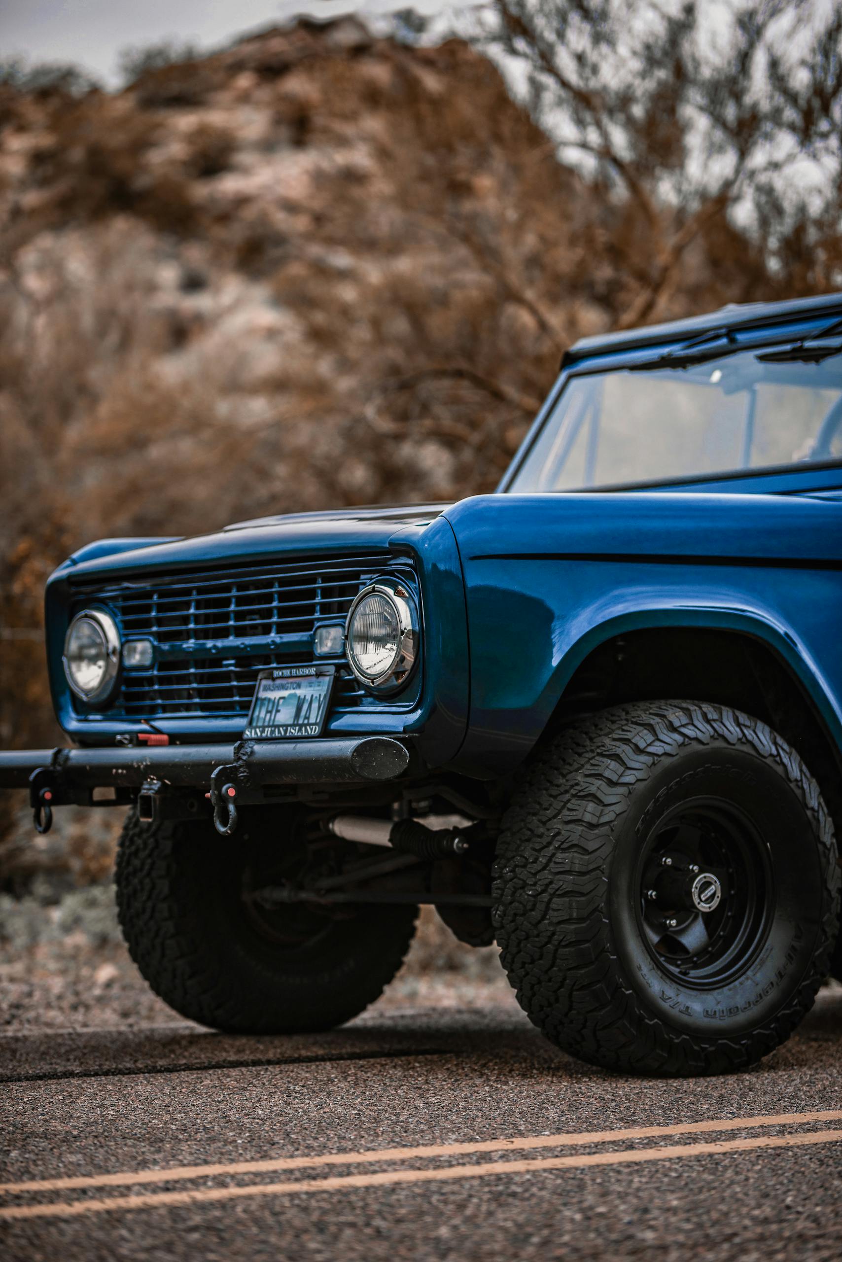 Vintage blue car captured on a scenic road with rugged terrain as the backdrop.